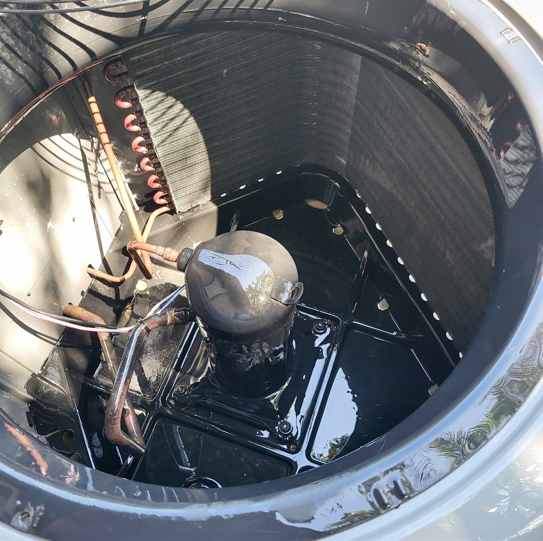 Close-up view inside an AC condenser unit showing the compressor and coil during service in Southwest Florida