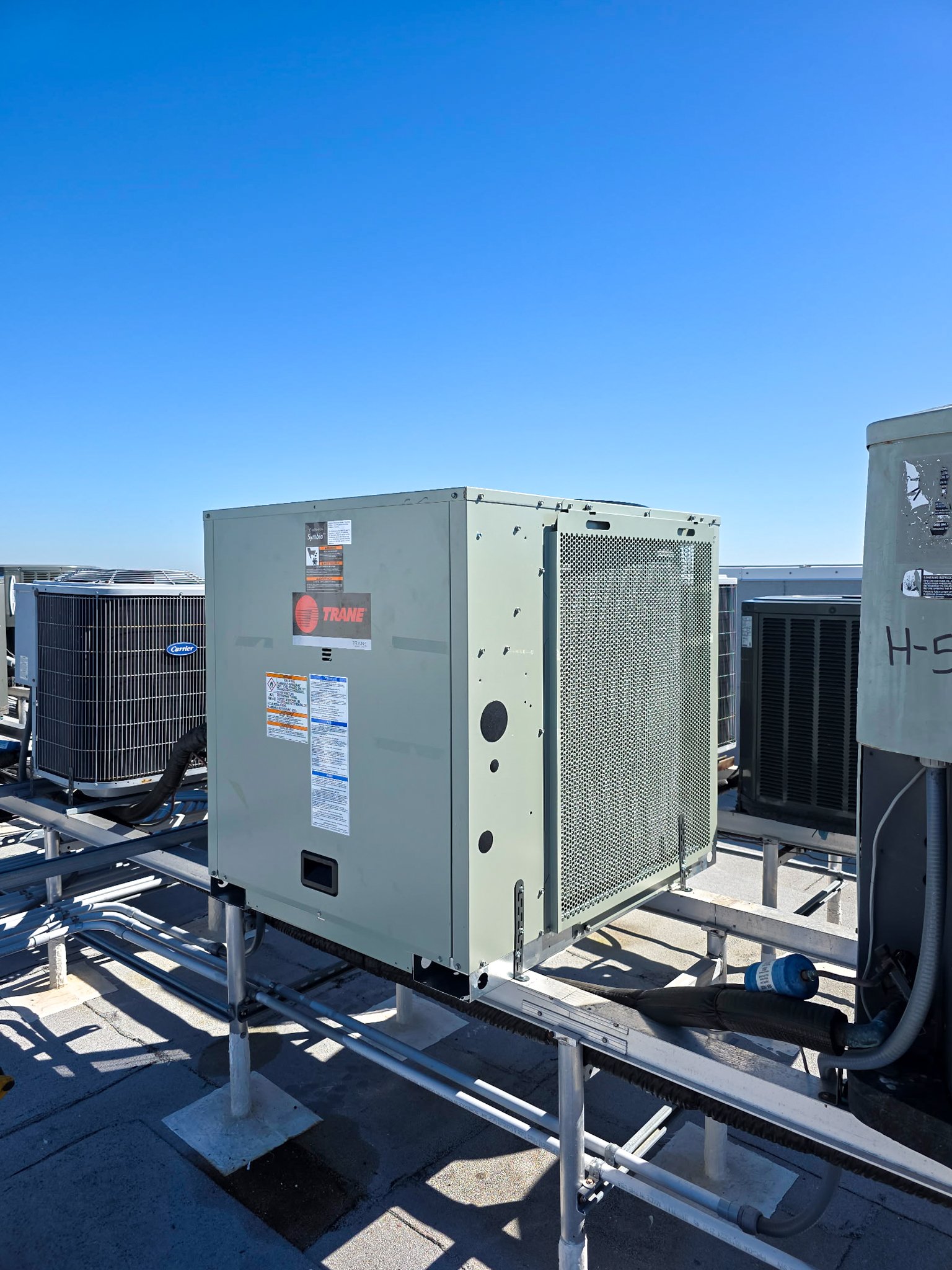 New Trane rooftop AC unit installed on a raised rack among other commercial condenser units