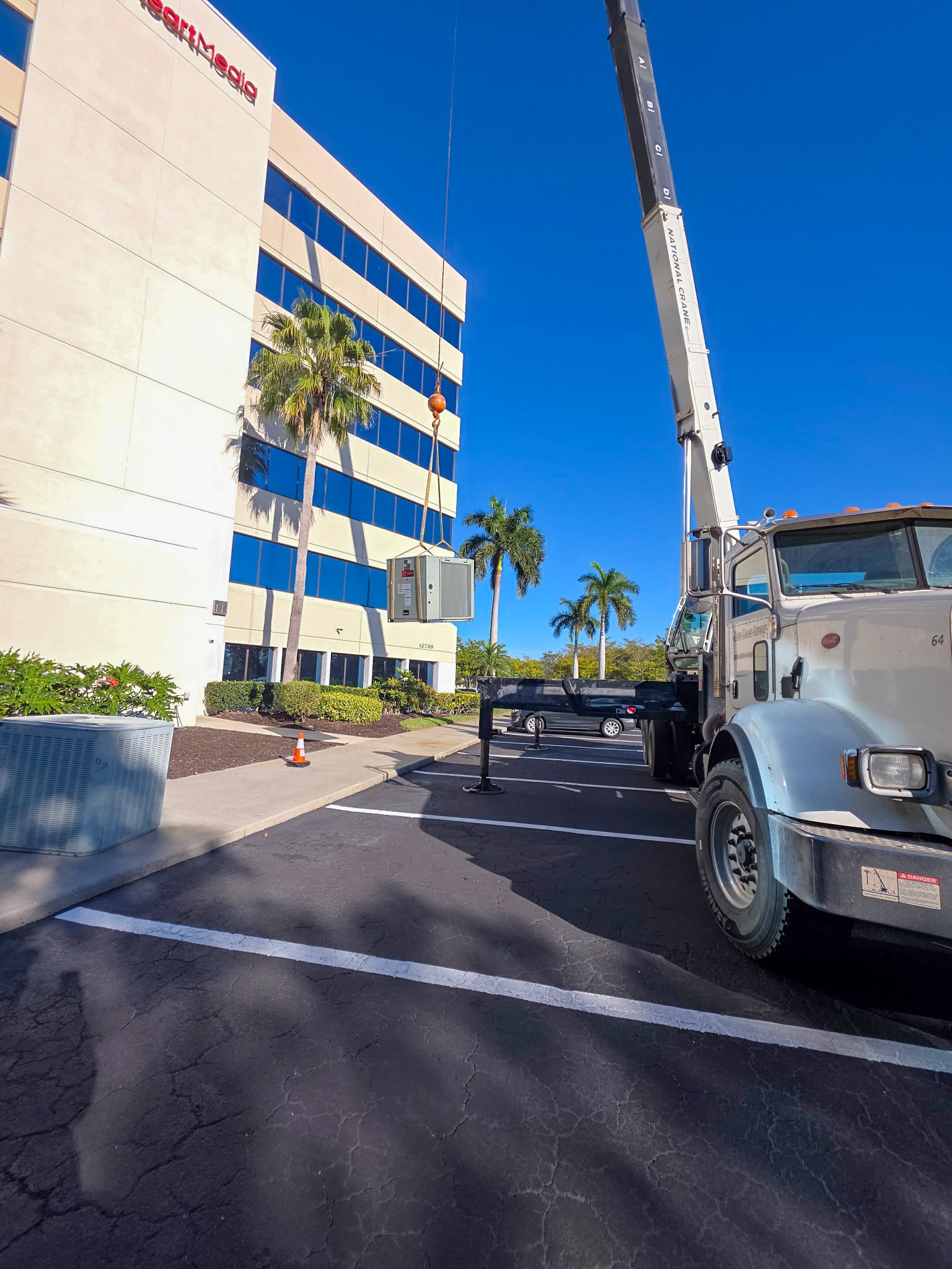 Crane lifting a rooftop AC unit for commercial installation at an office building in Southwest Florida